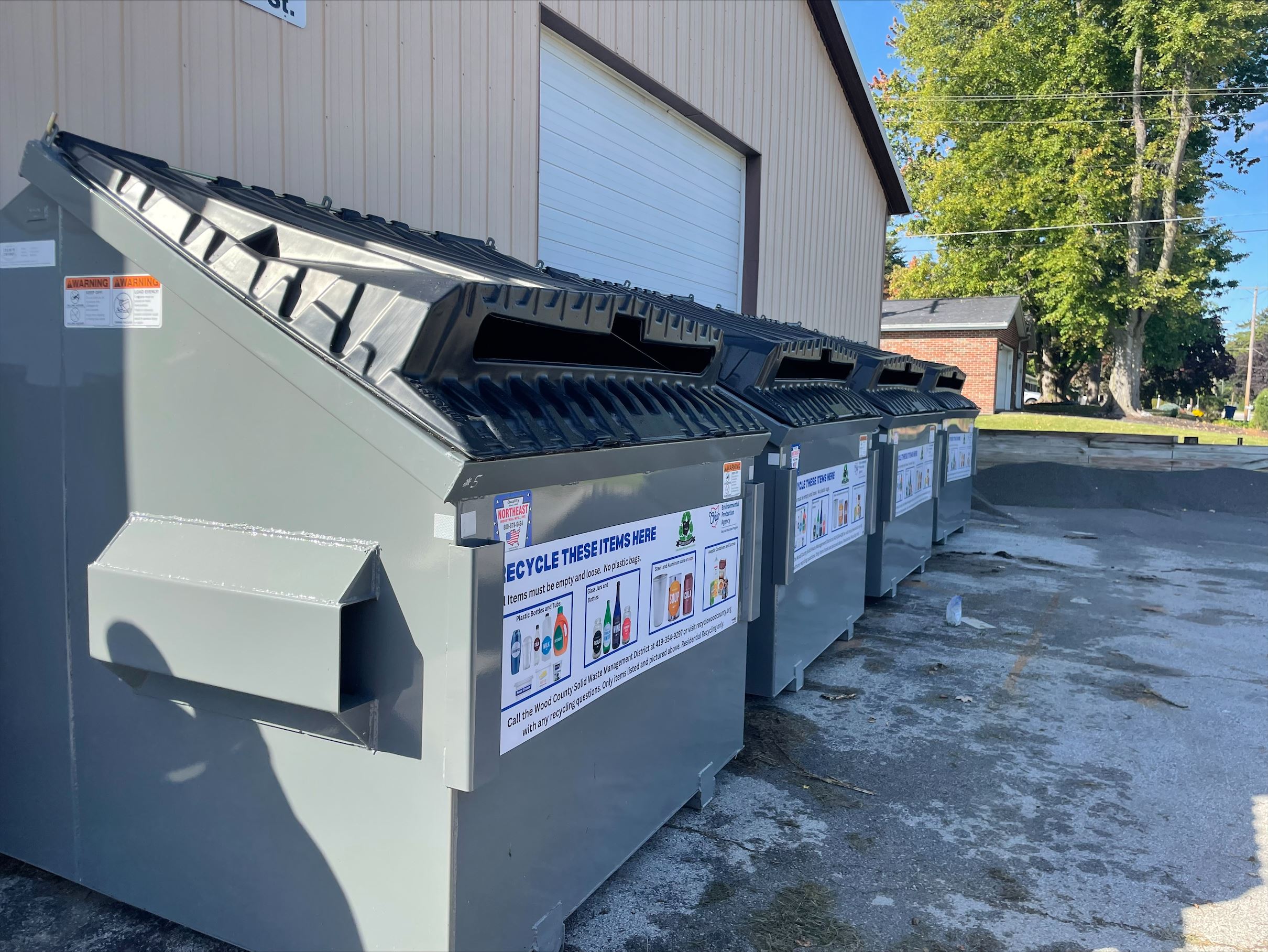 Four grey recycling drop-off dumpsters with CleanStream recycling lids. 
